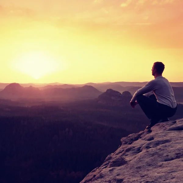 Adult in black trousers, jacket sit on cliff's edge — Stock Photo, Image