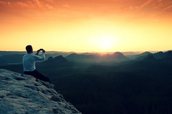 Gri t-shirt turist fotoğraf ile smartphone üzerinde kayalık tepe alır. — Stok fotoğraf