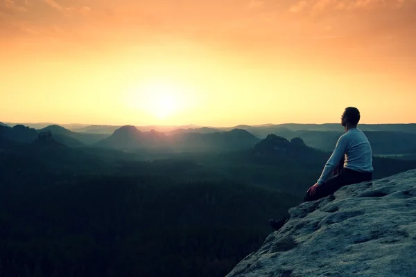 Man sit on peak. Colorful mist and fog in forest valley bellow. — Stock Photo, Image