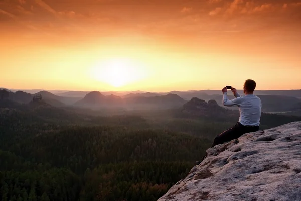 Tourist in grey t-shirt takes photos with smartphone on rocky peak — Stock Photo, Image