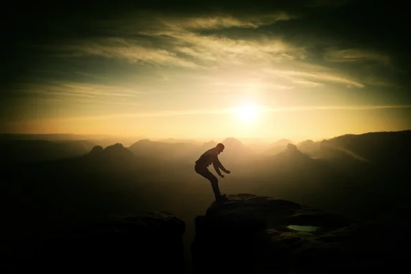 Pazzo escursionista che salta tra le rocce. Splendido tramonto colorato in montagne rocciose, pesante nebbia arancione in valle profonda. Miracolo della natura — Foto Stock