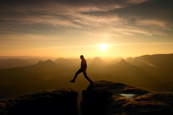 Un excursionista loco saltando entre rocas. Maravilloso amanecer colorido en las montañas rocosas, niebla naranja pesada en el valle profundo. Milagro de la naturaleza — Foto de Stock