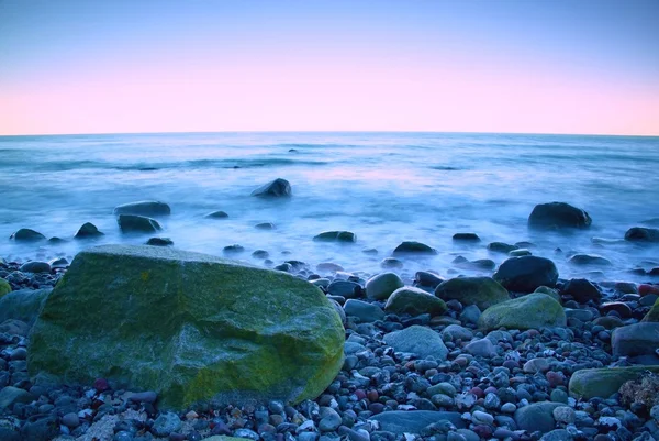 Mañana romántica en el mar. Grandes rocas que sobresalen del nivel del agua suave. Horozon rosa con los primeros rayos de sol caliente . — Foto de Stock