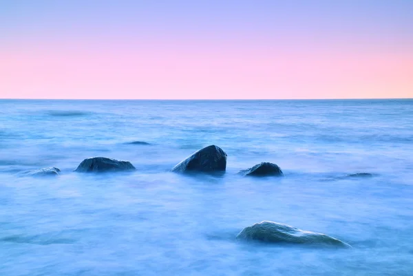 Matin romantique en mer. De gros blocs sortent du niveau d'eau lisse. Horozon rose avec premiers rayons chauds du soleil . — Photo