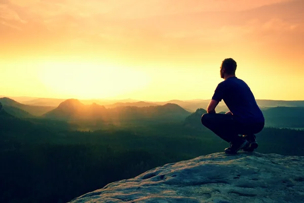 Toerist in gehurkte positie op peak van zandsteen rock en kijken in de vallei — Stockfoto