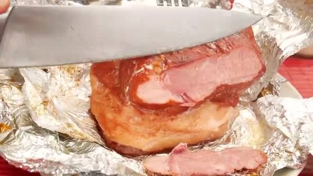 Close-up van de hand met chrome lang en scherp mes snijden gebraden varkensvlees ham in aluminiumfolie op gesneden bord. — Stockvideo