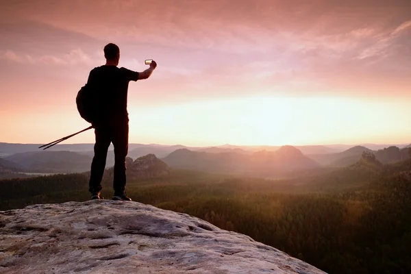 Forte escursionista uomo scattare foto selfie con smart phone in vetta alla montagna. Splendida alba . — Foto Stock