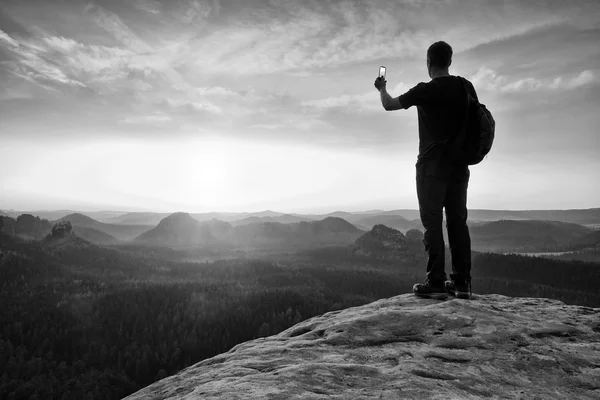 Hoog backpacker met telefoon in de hand. Lente daybreak in Bergen. — Stockfoto