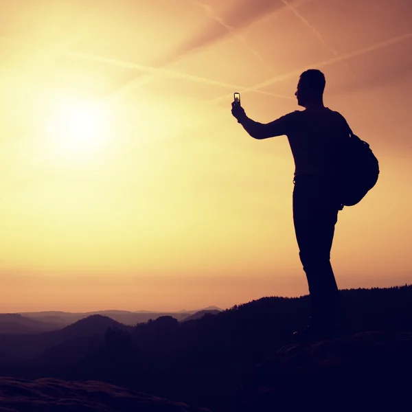 Tall backpacker with phone in hand. Spring daybreak in mountains. — Stock Photo, Image