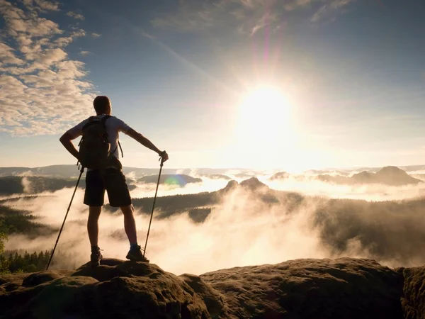 Турист со спортивным рюкзаком на скалистой точке обзора над туманной долиной. Воскресный день — стоковое фото