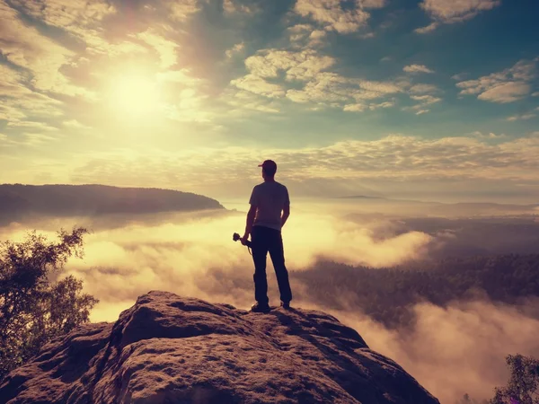 Fotografo con treppiede con macchina fotografica in piedi mani su punto di vista roccioso — Foto Stock