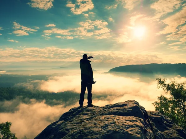 Фотограф с штативом на скале затеняет глаза и мышление. Тяжелый туманный пейзаж , — стоковое фото