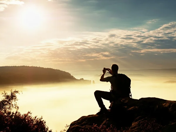 Verträumte Nebellandschaft. Amateurfotograf macht beeindruckende Fotos mit dem Handy. Wanderer mit Rucksack auf Klippe Photographie orange rosa nebligen Sonnenaufgang in einem schönen Tal unten — Stockfoto