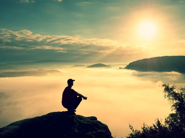 Момент одиночества. Человек сидит на скале и смотрит в красочный туман и туман в долине . — стоковое фото