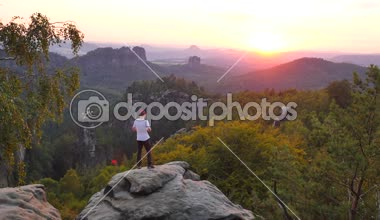 Turist gri gömlek ve trekking pantolon fotoğraf. Rock İmparatorluğu park zirve üzerinde fotoğraf ya da akıllı telefon ile video kaydetmek gerektirir. Yaz günbatımı güzel vadi Saksonya'nın İsviçre Parkı yukarıda. 