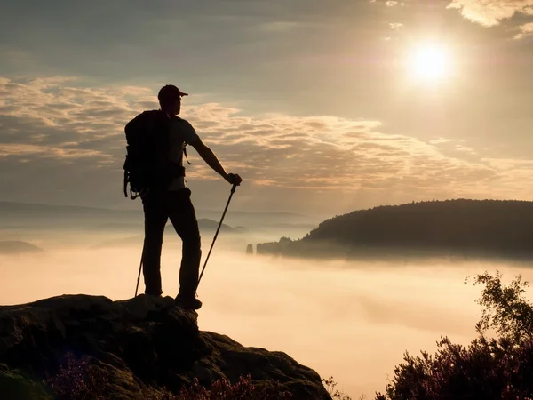 Hiker guide with sporty backpack and poles in hands. Misty spring daybreak