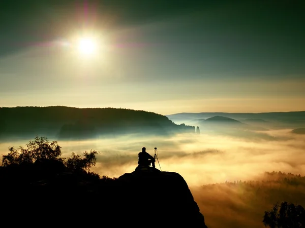 Fotografo con treppiede e macchina fotografica su scogliera e pensiero. Paesaggio nebbioso da sogno — Foto Stock