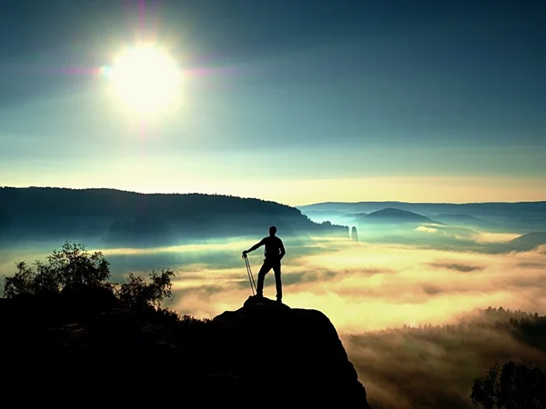 Mochilero alto con bastones en la mano. Soleado amanecer brumoso en las rocas — Foto de Stock