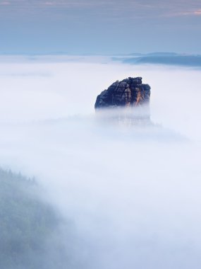 Sharp sandstone rock empire sticking out from heavy fog. Deep misty valley clipart