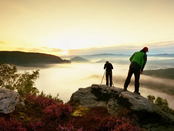 Hiker look down into fogy valley. Photographer stay on cliff and takes photos. — Stock Photo, Image