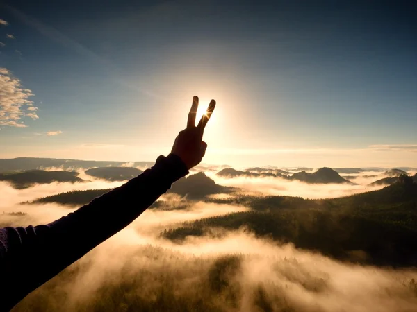 La mano del hombre hace la victoria al Sol. Amanecer brumoso en las montañas — Foto de Stock