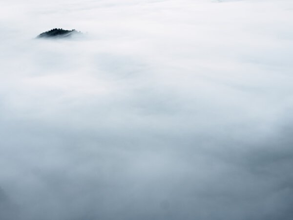 Темная вершина холма торчит из густого тумана. Глубокая туманная долина, полная сливочного тумана
