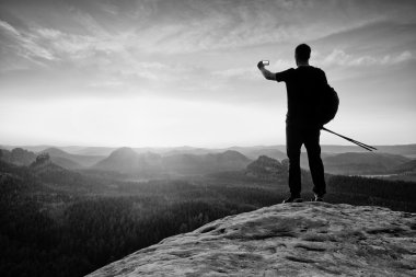 Güçlü adam otostopçu dağ zirvesinde akıllı telefon ile fotoğraf çekmek. Harika bir gün molası. Siyah beyaz fotoğraf