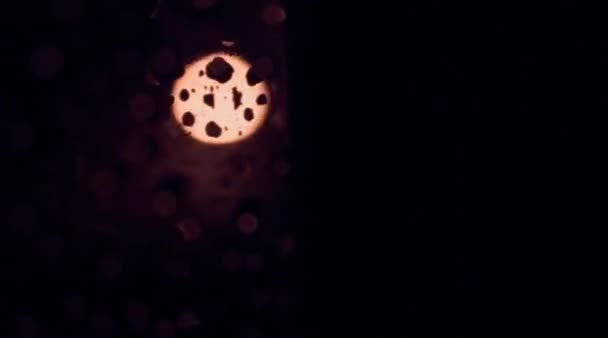 Luz de la ciudad nocturna abstracta sobre una ventana húmeda con gotas de lluvia brillantes. Movimiento del vidrio, cambio suave de profundidad de campo. Caducidad — Vídeo de stock