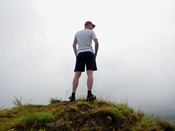 Man in cloud of fog. Hiker in white black with  red cap stand on peak . — Stock Photo, Image