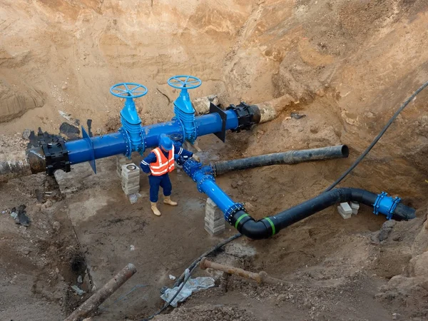 Technical expert underground at gate valve on 500mm drink water pipes joined with new black waga multi joint members into old pipeline system. Check of repaired before covering. Asphalt isolation