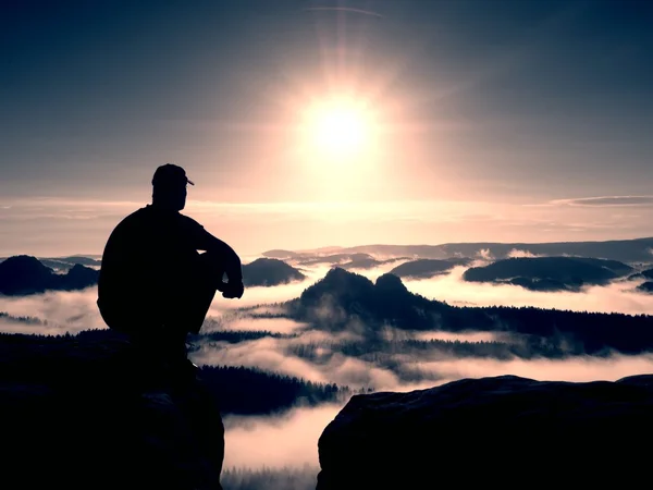 Moment of loneliness. Man with cap sit on mountain and watch to fog — Stock Photo, Image