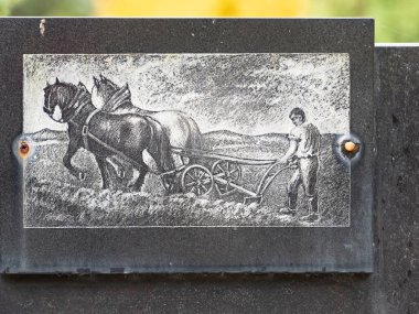 20. yüzyılın başlarından bir toprak sahibinin taş mezarı. 24 Ekim 2020. Hronov mezarlığı, Çek. İki sağlam at tarafından çekilen sabanın arkasındaki yaşlı bir adamın oymalı resmi.. 