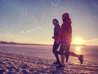 Kadın koşucu ve koçu kış güneşli havalarda plajda koşuyorlar. Soyut filtre.