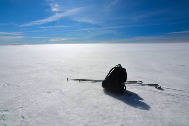 Kros kayak direkleri ve sırt çantası kayak pistinde buzlu kar örtüsünün üzerinde yatıyordu. Açık mavi kış gökyüzü.