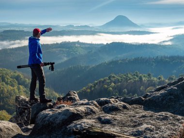 Silüetli fotoğrafçı tripodda kamera taşıyor. Doğal fotoğrafçı kamerayı tripodla tutar ve sisli dağ vadisine bakar.