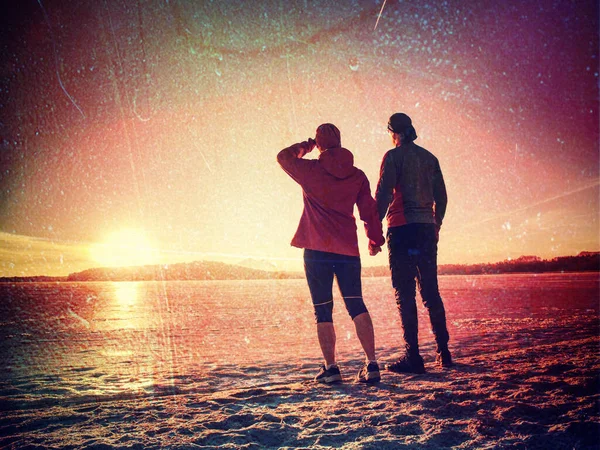 爱运动伴侣手牵手望着冬季海滩上冰冷的大海的后视镜 — 图库照片