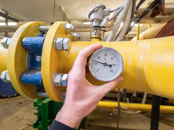 Controler hold in hand temperature gauges on yellow sludge pipe in wastewater company.  Underground pumping station.