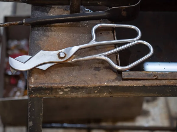 Shaped Blowing Glass Diamond Shear Scissors on a Metal Table. Detailed glassblower tools in workshop