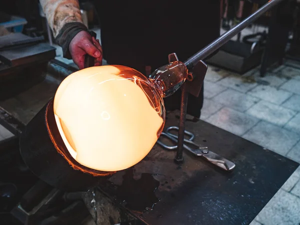 Glass blower forming hot piece of glass with wooden tool. Traditional glass crafter works with  burning and blowing an art piece. Hand made glass studio in Kunratice.