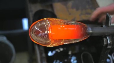 Cam üfleyici eriyen camlara üflüyor ve beyaz katman ekliyor. Sanatçı geleneksel yöntemle cam üfleme borusunda kırmızı parlak camlar oluşturuyor.. 