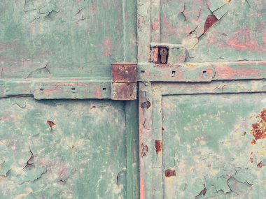 Kapı mandalı kilitlenmiş ve güvenlik kilidi takılmış eski yeşil bir kapı. Paslı lekeli çatlak boyalı yüzey