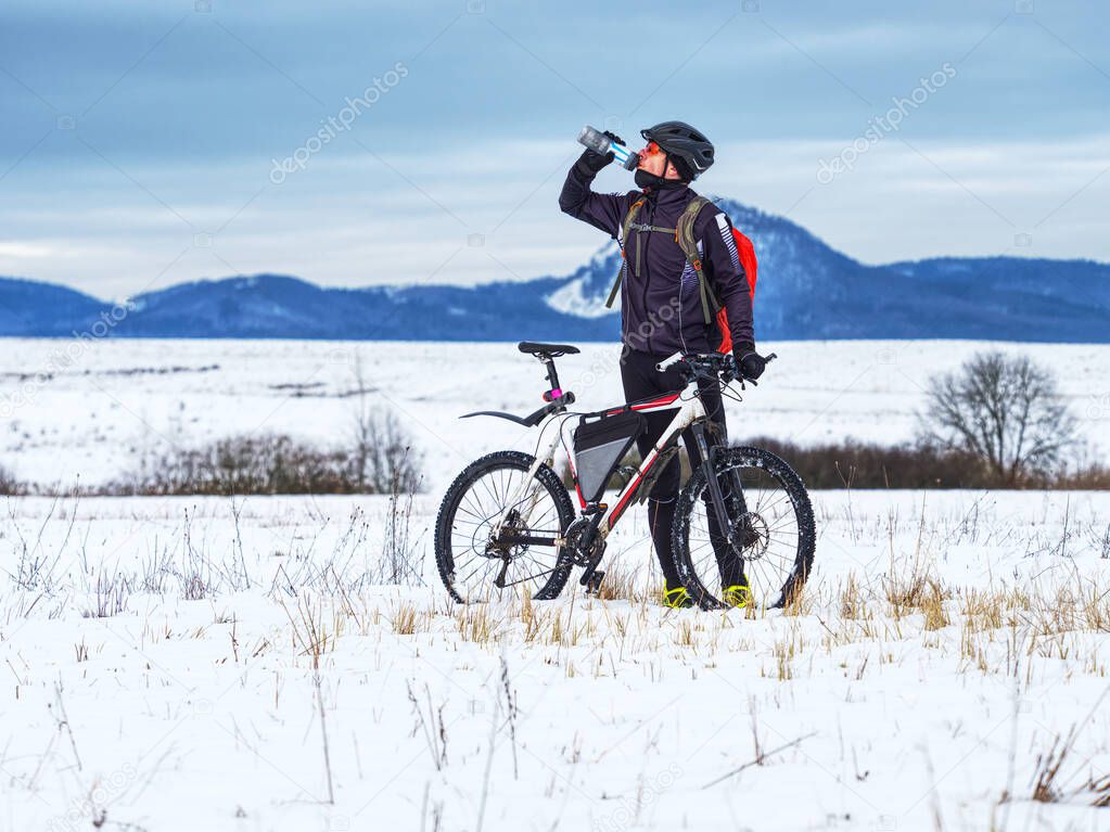 Extreme cyclist stopped the winter training and drinks a refreshing drink from a thermos. Challenging winter terrain with his white fatbike.