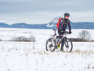 Erkek dağ bisikletçisi kışın karlı kır yolunda yürüyor. MTB 'yi kar altında iten bisikletçi