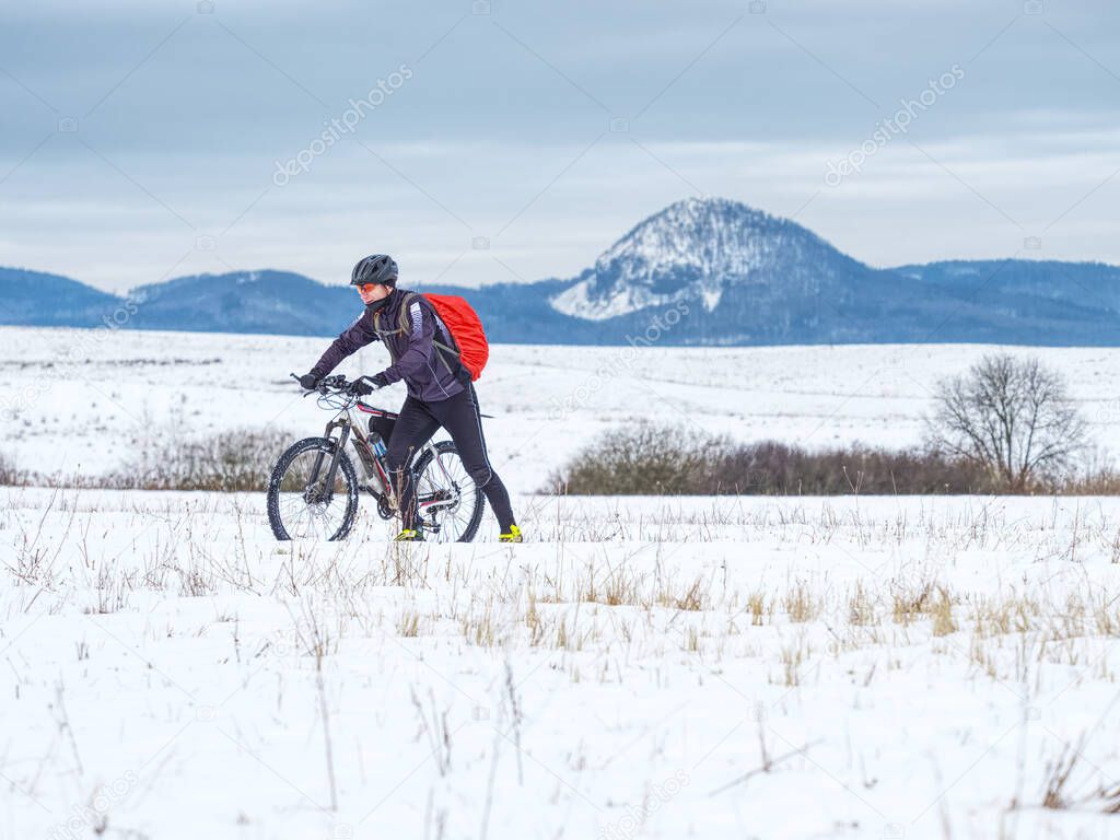 Mountain biker in snowy landscape. Sportsman properly equiped for winter cycling is ridding in heavy terrain.  Sunny winter weather and snow.