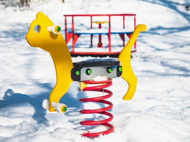 Oyun parkında kar altında bir yayda atlayan at. Sessiz terk edilmiş oyun alanı.