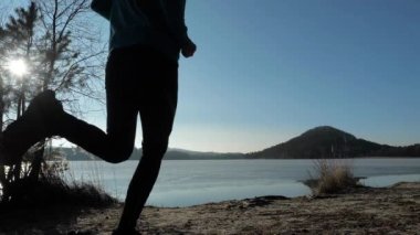 Spor giyimli çağdaş genç adam sabahları sahilde kıyı şeridi boyunca koşuyor. Düşük açı. Yavaş çekim.
