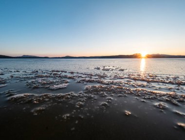 Göl koyunda buzun erimesi. Parlak beyaz bir buz kütlesinin altından eriyen portakal mavisi suyun sınırı..