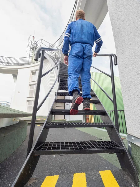 Employee walk upstairs in factory. Man in safety wearing going up on steel ladder. Rear view.