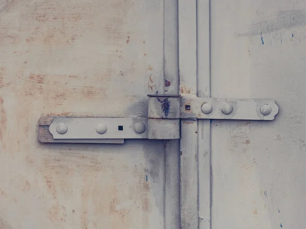 Locked industrial door. Rusty padlock hasp welded on metal sheet door and small locking insert. Cracked vintage grey brown paint.