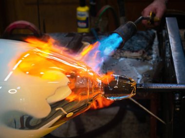 Glass artist fires a glass ball with a gas torch so that he can shape it by hand. Traditional method of shaping molten glass. Slow motion. clipart